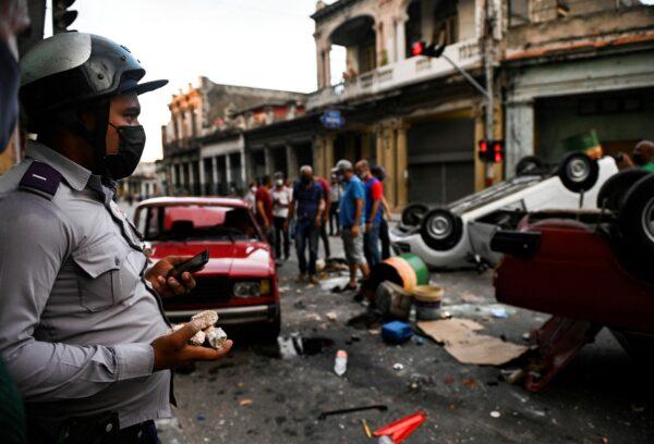 A policeman stands while watching police cars overturned in the street in the framework of a demonstration against Cuban President Miguel Diaz-Canel in Havana, on July 11, 2021. (Yamil Lage/AFP via Getty Images)