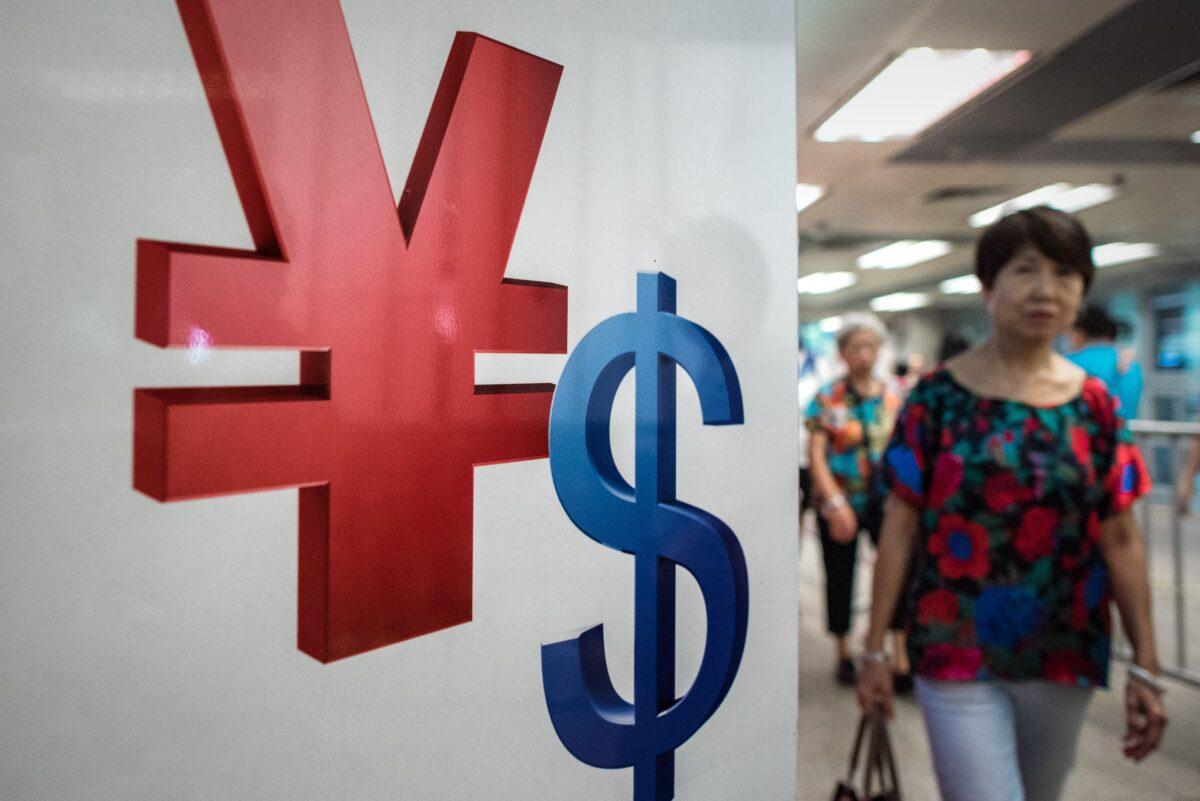 A woman walks past a yuan and a U.S. dollar currency sign in Hong Kong on Aug. 13, 2015. (Philippe Lopez/AFP via Getty Images)