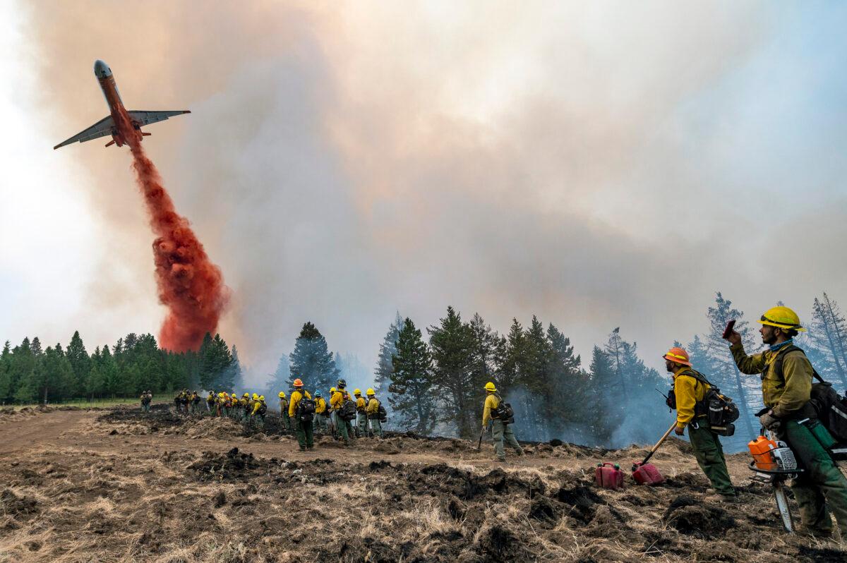 Wildland firefighters watch and take video with their cellphones as a plane drops fire retardant on Harlow Ridge above the Lick Creek Fire, southwest of Asotin, Wash., on July 12, 2021. (Pete Caster/Lewiston Tribune via AP)