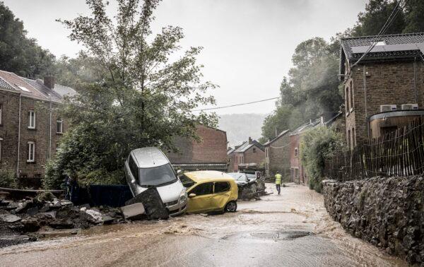 A man walks by damaged cars in a flooded street in Mery, Province of Liege, Belgium, on July 14, 2021. (Valentin Bianchi/AP Photo)