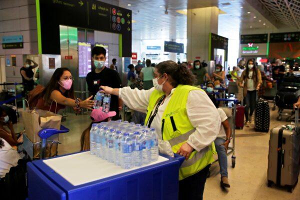 An airport worker hands out water bottles to passengers queueing at Lisbon airport, Portugal on July 17, 2021. (Armando Franca/AP Photo)