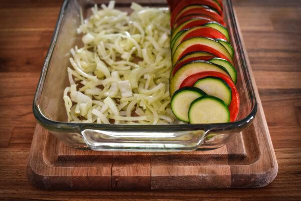 Arrange the tomato, zucchini, and eggplant slices on top of the onions in tightly packed rows. (Audrey Le Goff)