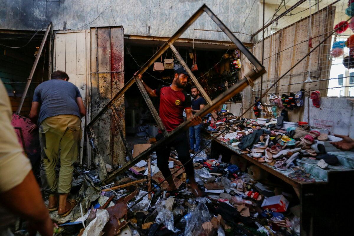 People pick up debris at the site of an explosion in Sadr City district of Baghdad, Iraq, on July 19, 2021. (Wissam Al-Okaili/Reuters)