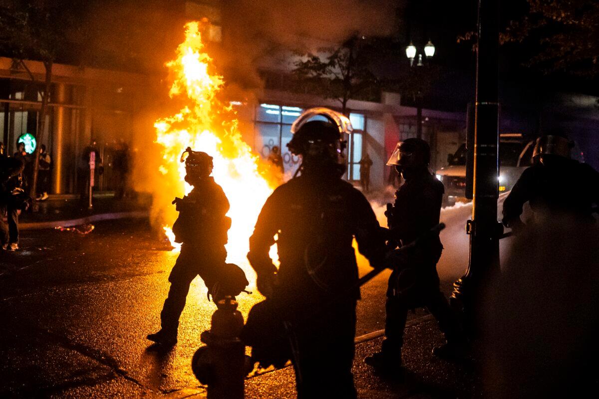 Portland police officers walk past a fire started by a Molotov cocktail that a rioter hurled at them, in Portland, Ore., on Sept. 23, 2020. (Nathan Howard/Getty Images)