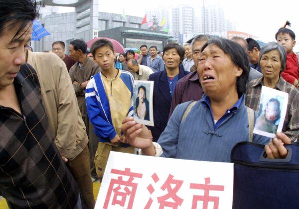 A woman cries as she holds photos of her son, who she alleged was brutalized and killed by the local officials, as she joins other petitioners lining up outside the new complaints bureau in Xian, Shaanxi Province, China, on Aug. 18, 2005, for a chance to submit their grievances. (STR/AFP via Getty Images)