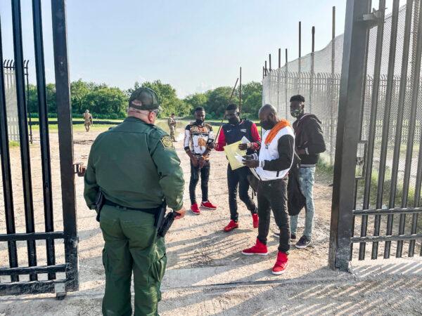 A Border Patrol agent picks up four illegal immigrants from Haiti who have just crossed the Rio Grande from Mexico into Del Rio, Texas, on July 21, 2021. (Charlotte Cuthbertson/The Epoch Times)