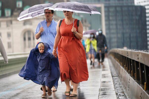 A young family walk over Westminster Bridge as heavy rain sweeps through central London on July 25, 2021. (Victoria Jones/PA)