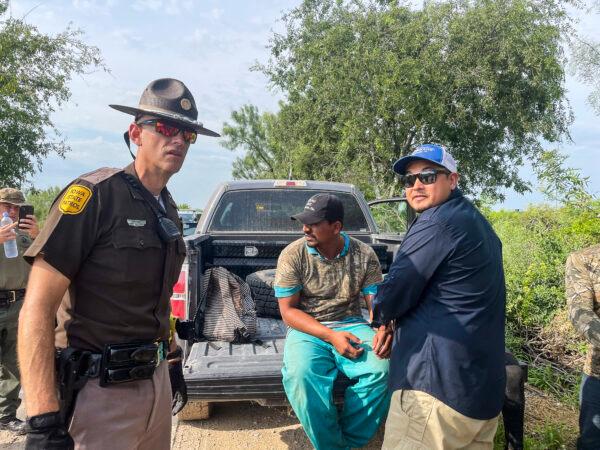 An Iowa State Trooper (L) assists Border Patrol in detaining illegal immigrants from Honduras and Guatemala while deployed to Texas, in Kinney County, Texas, on July 21, 2021. (Charlotte Cuthbertson/The Epoch Times)