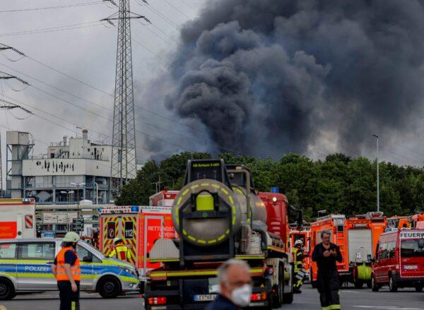 Emergency vehicles of the fire brigade, rescue services and police stand not far from an access road to the Chempark over which a dark cloud of smoke is rising in Leverkusen, Germany, on July 27, 2021. (Oliver Berg/dpa via AP)