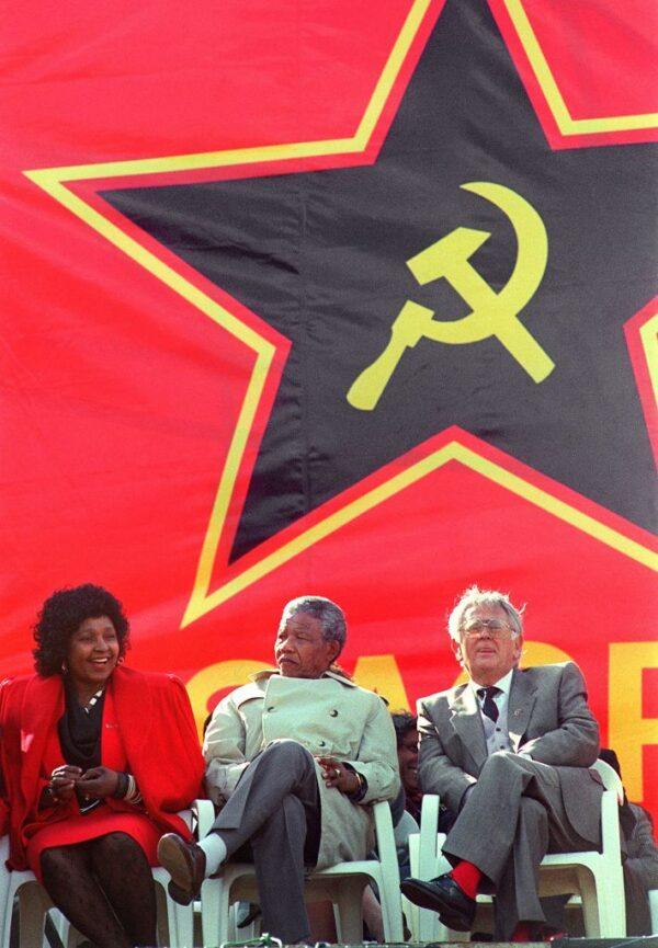 South African anti-apartheid leader and African National Congress (ANC) member Nelson Mandela (C), his then-wife Winnie (L) and Joe Slovo (R), South African Communist Party (SACP) leader are seated on July 29, 1990 in Soweto on the platform at a SACP’s meeting, during its official launch as a political party in South Africa. (Walter Dhladhla/AFP via Getty Images)