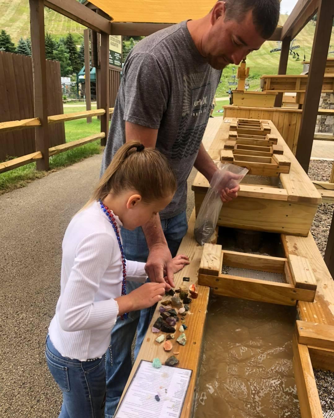 A father and daughter enjoy gem mining by sifting and shaking a tray in a sluice box with water to reveal various colorful treasures. (Courtesy of Seven Springs)