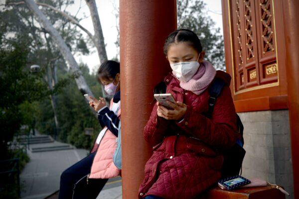 Two students look at their cell phones as they sit under a pavilion in heavy smog near the Forbidden City in Beijing, China on Nov. 4, 2016. (Wang Zhao/AFP via Getty Images)