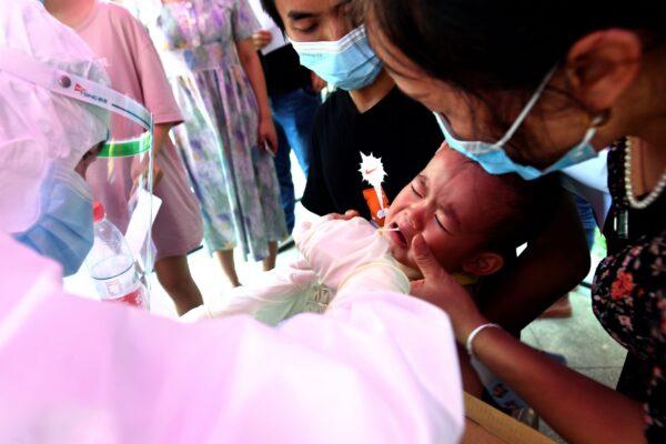 A medical worker takes swab samples from a child during mass testing for COVID-19 at a residential block in Wuhan, Hubei province, China, on Aug. 3, 2021. (Chinatopix via AP)