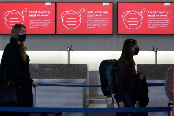 Signs advising facial covering requirements are shown as travelers stand in line at a Delta Air Lines desk at San Francisco International Airport in San Francisco, on Dec. 22, 2020. (AP Photo/Jeff Chiu)