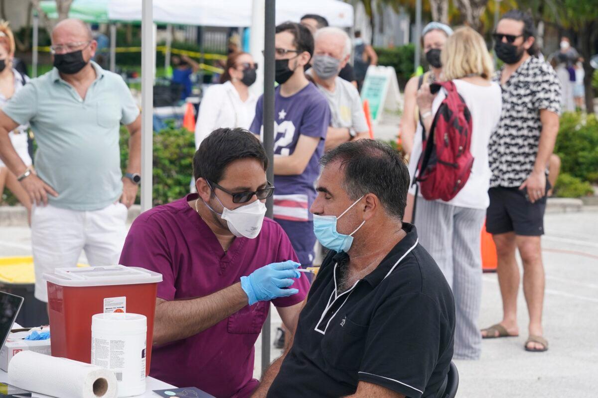 Carlos Anacleto closes his eyes as he receives the Pfizer COVID-19 vaccine from nurse Jorge Tase, as others wait in line, in Miami Beach, Fla., on Aug. 4, 2021. (Marta Lavandier/AP Photo)