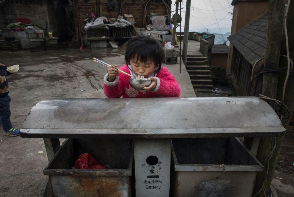A young girl of the Long Horn Miao ethnic minority group eats food on top of a garbage bin in a housing area that is part of a tourism project after Tiaohua or Flower Festival as part of the Lunar New Year in Longga village, Guizhou province, southern China, on Feb. 7, 2017. (Kevin Frayer/Getty Images)