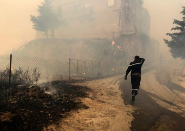 A civil protection rescue worker walks near smoke rising from a forest fire in the mountainous Tizi Ouzou province, east of Algiers, Algeria on Aug. 10, 2021. (Abdelaziz Boumzar/Reuters)