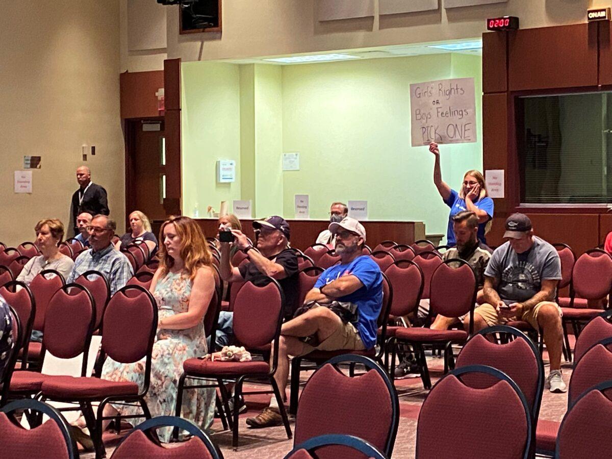 A woman holds a sign as board member Jeff Morse speaks at the Loudoun County Public Schools board meeting in Virginia on Aug. 11, 2021. (Terri Wu/The Epoch Times)