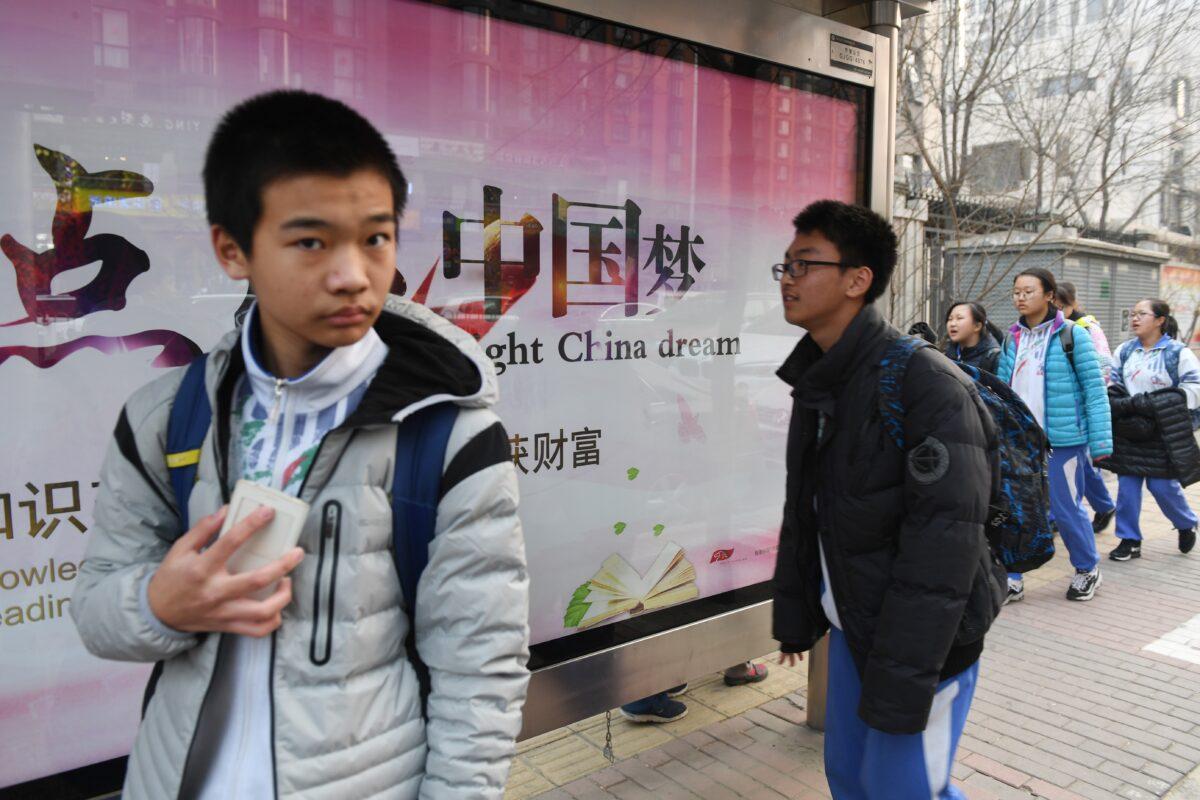 Youths walk past a propaganda billboard about the "China Dream," a slogan associated with Chinese regime leader Xi Jinping, outside a school in Beijing on March 12, 2018. (Greg Baker/AFP via Getty Images)