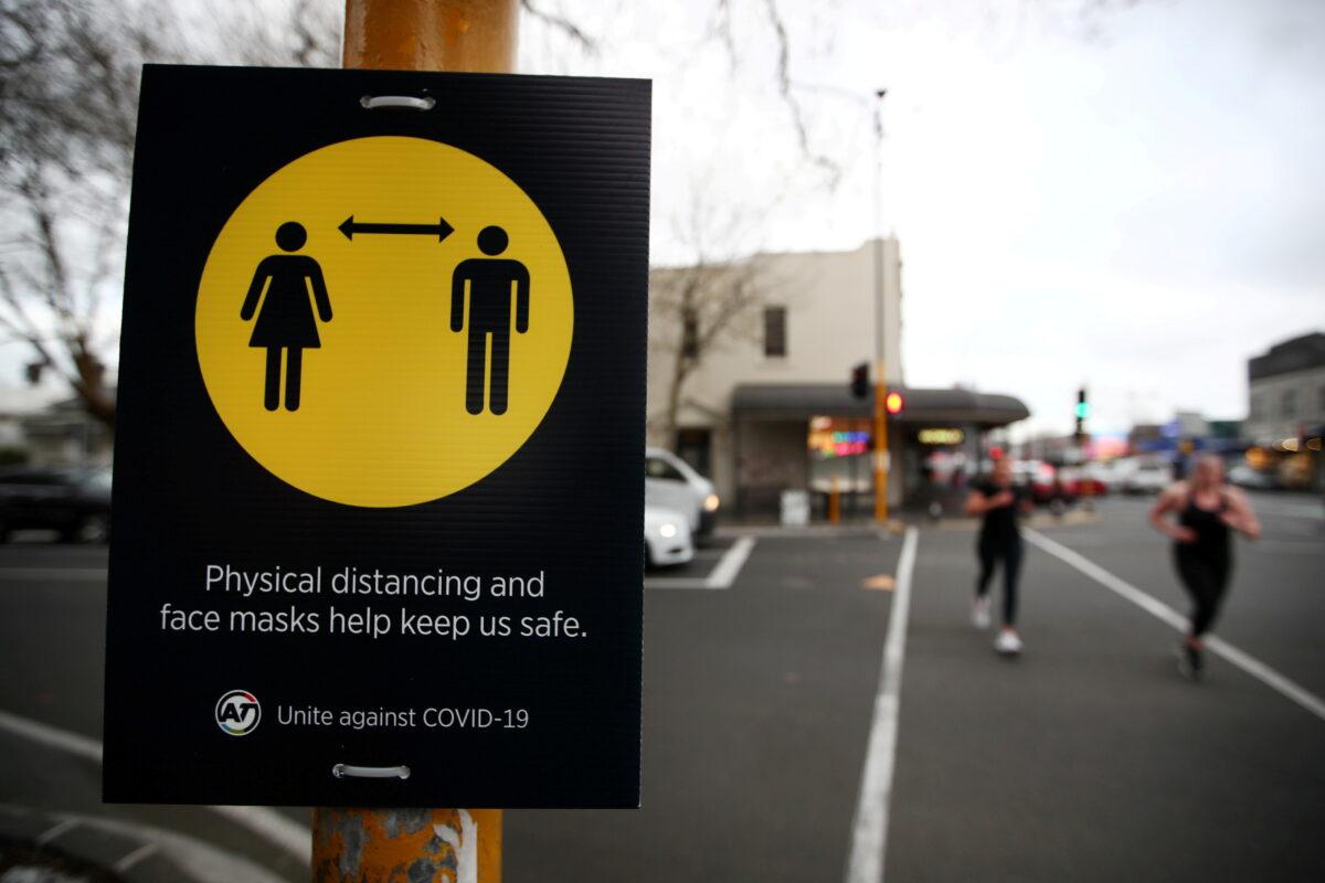 People jog past a social distancing sign on the first day of New Zealand's new COVID-19 safety measure that mandates wearing of a mask on public transport, in Auckland, New Zealand on Aug. 31, 2020. (Fiona Goodall/Reuters)