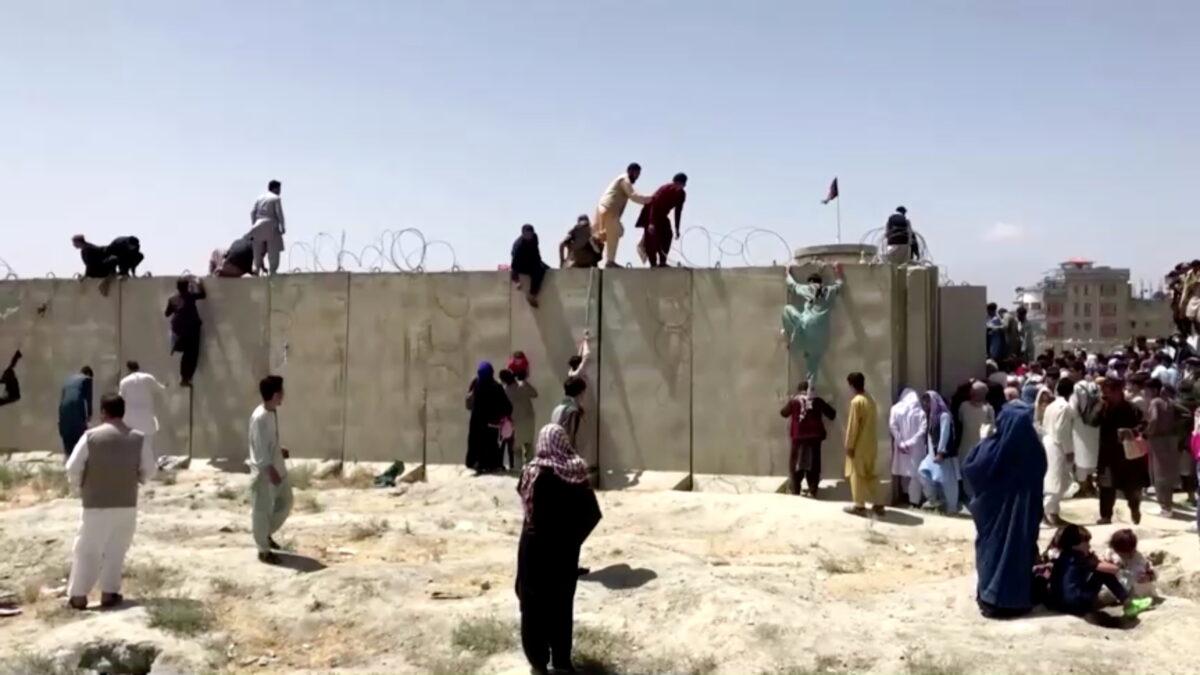 In this still image taken from a video, people climb a barbed wire wall to enter the airport in Kabul, Afghanistan, on Aug. 16, 2021. (Reuters TV/via Reuters)