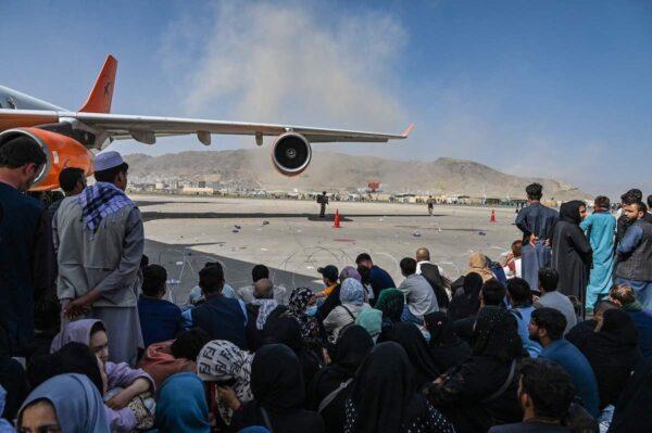 Afghan people sit as they wait to leave Kabul airport on Aug. 16, 2021. After a stunningly swift end to Afghanistan's 20-year war, thousands of people mobbed the city's airport trying to flee Taliban terrorists. (Wakil Kohsar/AFP via Getty Images)