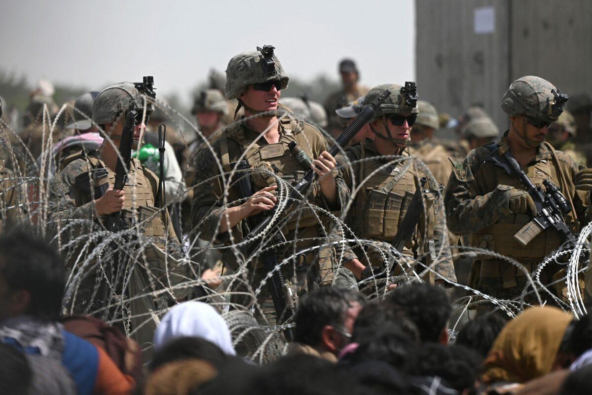 U.S. soldiers stand guard behind barbed wire as Afghans sit on a roadside near the military part of the airport in Kabul, Afghanistan, on Aug. 20, 2021. (Wakil Kohsar/AFP via Getty Images)