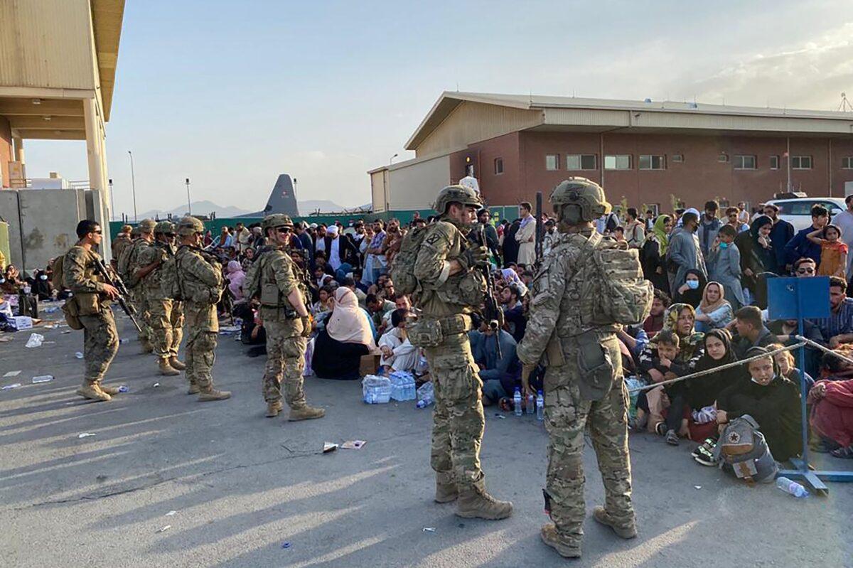 U.S. soldiers stand guard as Afghan people wait to board a U.S. military aircraft to leave Afghanistan, at the military airport in Kabul on August 19, 2021. (Shakib Rahmani/AFP via Getty Images)