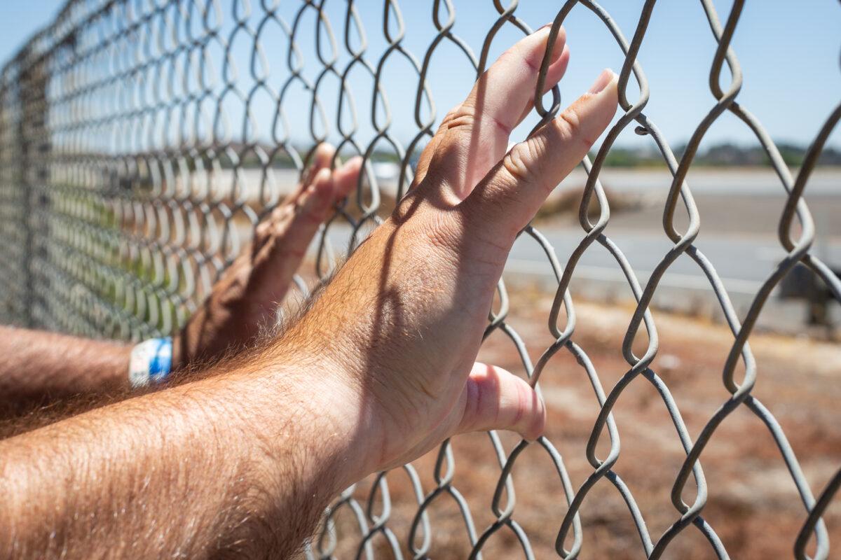 Jim R. places his hands on a chain-link fence in Lake Forest, Calif., on Aug. 4, 2021. (John Fredricks/The Epoch Times)
