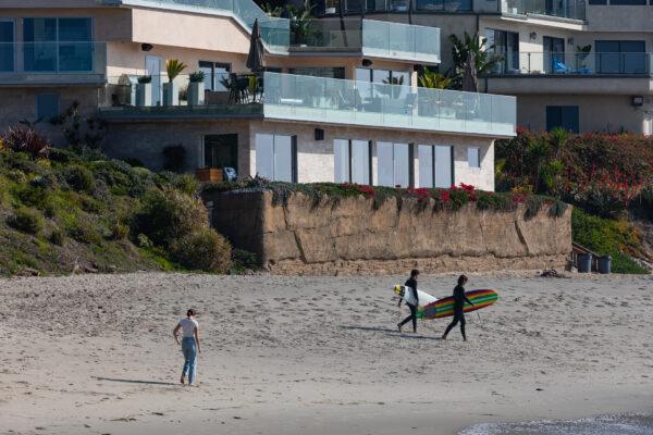 Surfers walk past a seawall built in front of a home at Victoria Beach, in the city of Laguna Beach, Calif., on Jan. 8, 2021. (John Fredricks/The Epoch Times)