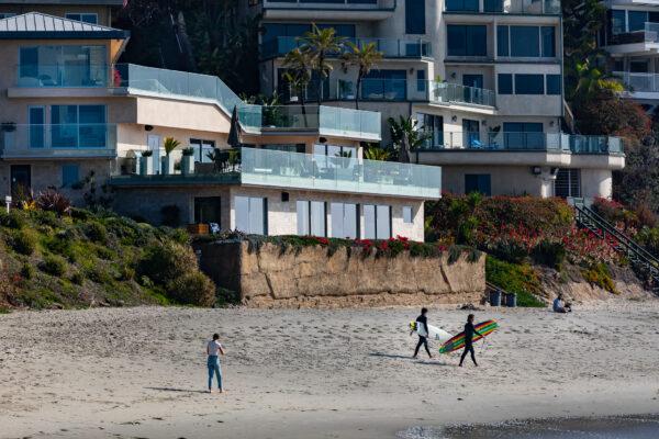 Surfers walk past a seawall built in front of a home at Victoria Beach, in the City of Laguna Beach, Calif., on Jan. 8, 2021. (John Fredricks/The Epoch Times)