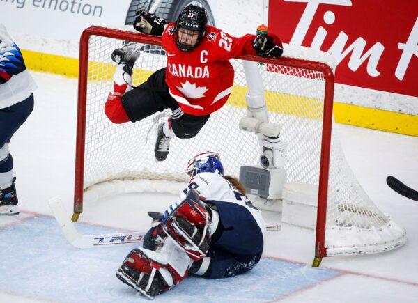 Canada's Marie-Philip Poulin (Top) hangs from the cross bar after crashing into U.S. goalie Nicole Hensley during the third period of the IIHF hockey women's world championships title game in Calgary, Alberta, Canada, on Aug. 31, 2021. (Jeff McIntosh/The Canadian Press via AP)