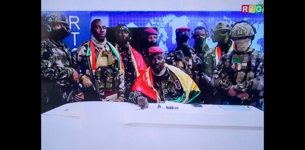 In this image made from video, Col. Mamadi Doumbouya (C) commander of the army's special forces unit, surrounded by others and draped in a Guinean flag, makes an address to the nation from state television headquarters in the capital Conakry, Guinea on Sept. 5, 2021. (Radio Television Guineenne via AP)