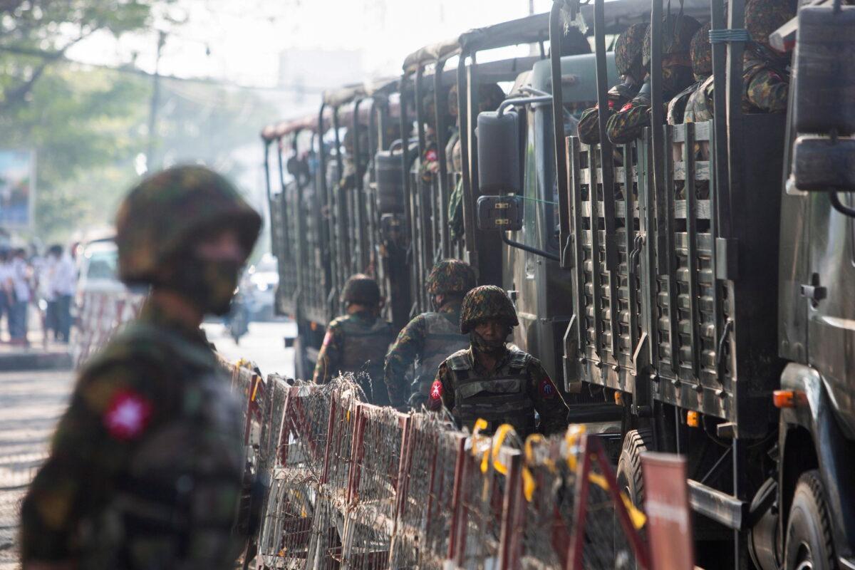 Soldiers stand next to military vehicles as people gather to protest against the military coup, in Yangon, Burma, on Feb. 15, 2021. (Stringer/Reuters)