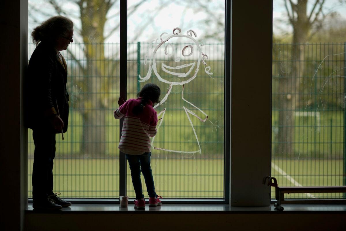 A young girl paints a picture of herself on the school window as children of key workers take part in school activities at Oldfield Brow Primary School in Altrincham, England, on April 8, 2020. (Christopher Furlong/Getty Images)