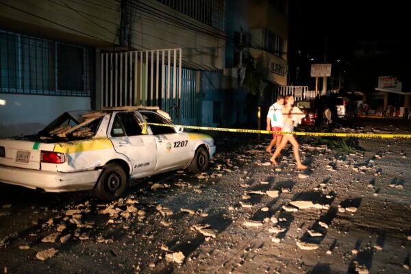 A couple walks past a taxi cab that was damaged by falling debris after a strong earthquake in Acapulco, Mexico, on Sept. 7, 2021. (Bernardino Hernandez/AP Photo)
