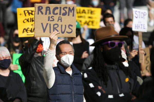 A man holds a sign that reads "Racism is a Virus" during the "We Are Not Silent" rally against anti-Asian hate in response to recent anti-Asian crime in the Chinatown-International District of Seattle, Washington on March 13, 2021. (Jason Redmond/AFP via Getty Images)