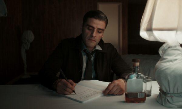 When not working, William Tell (Oscar Isaac) sits in his hotel room, covered in sheets, and writes. (Focus Features/Copyright 2021 Focus Features, LLC)