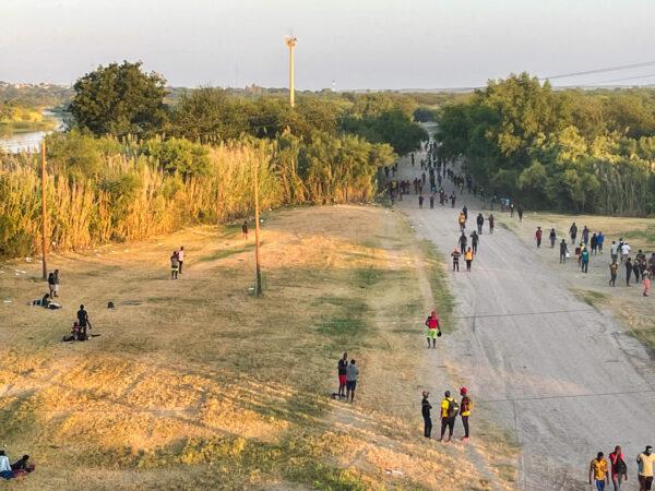 Illegal immigrants walk near the international bridge area after crossing the Rio Grande (on left), from Mexico into Del Rio, Texas, on Sept. 16, 2021. (Charlotte Cuthbertson/The Epoch Times)