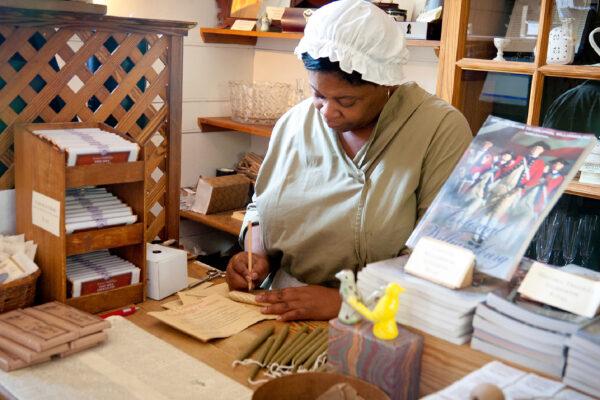 A shopkeeper in traditional attire shows visitors to Colonial Williamsburg, Va., how business was done in earlier days. (Aviahuismanphotography/Dreamstime.com)