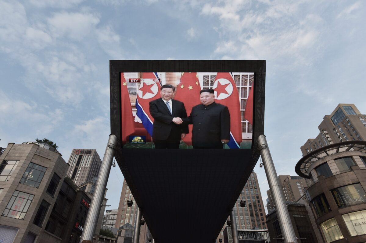 Chinese leader Xi Jinping (L) being greeted in Pyongyang by North Korean leader Kim Jong Un is shown on a large screen outside a shopping mall in Beijing on June 20, 2019. (Greg Baker/AFP)