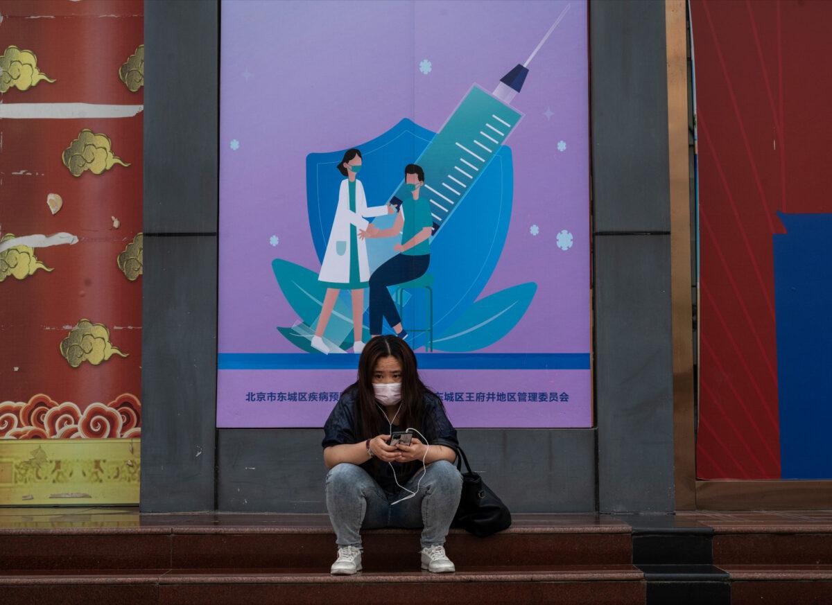 A woman wears a protective mask as she sits in front of a sign promoting a local government COVID-19 vaccination center in Beijing on May 23, 2021. (Kevin Frayer/Getty Images)