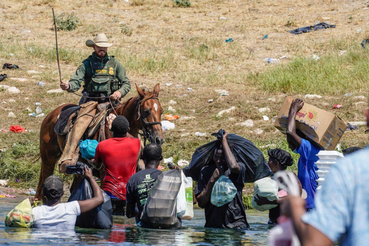 A United States Border Patrol agent on horseback faces off with illegal immigrants on the banks of the Rio Grande River at the U.S.-Mexico border in Del Rio, Texas, on Sept. 19, 2021. (Paul Ratje/AFP via Getty Images)