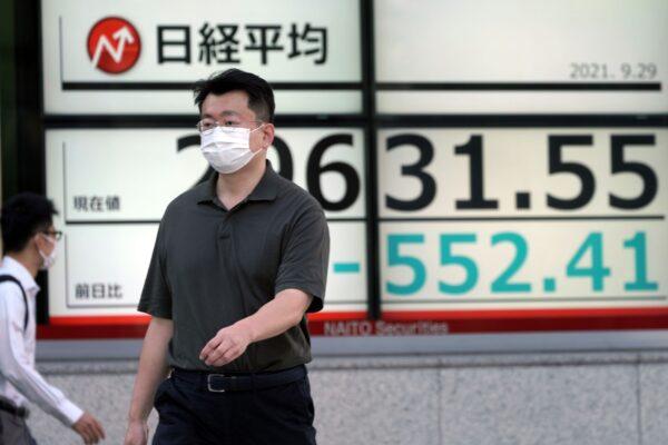 A man wearing a protective mask walks in front of an electronic stock board showing Japan's Nikkei 225 index at a securities firm in Tokyo, Japan on Sept. 29, 2021. (Eugene Hoshiko/AP Photo)