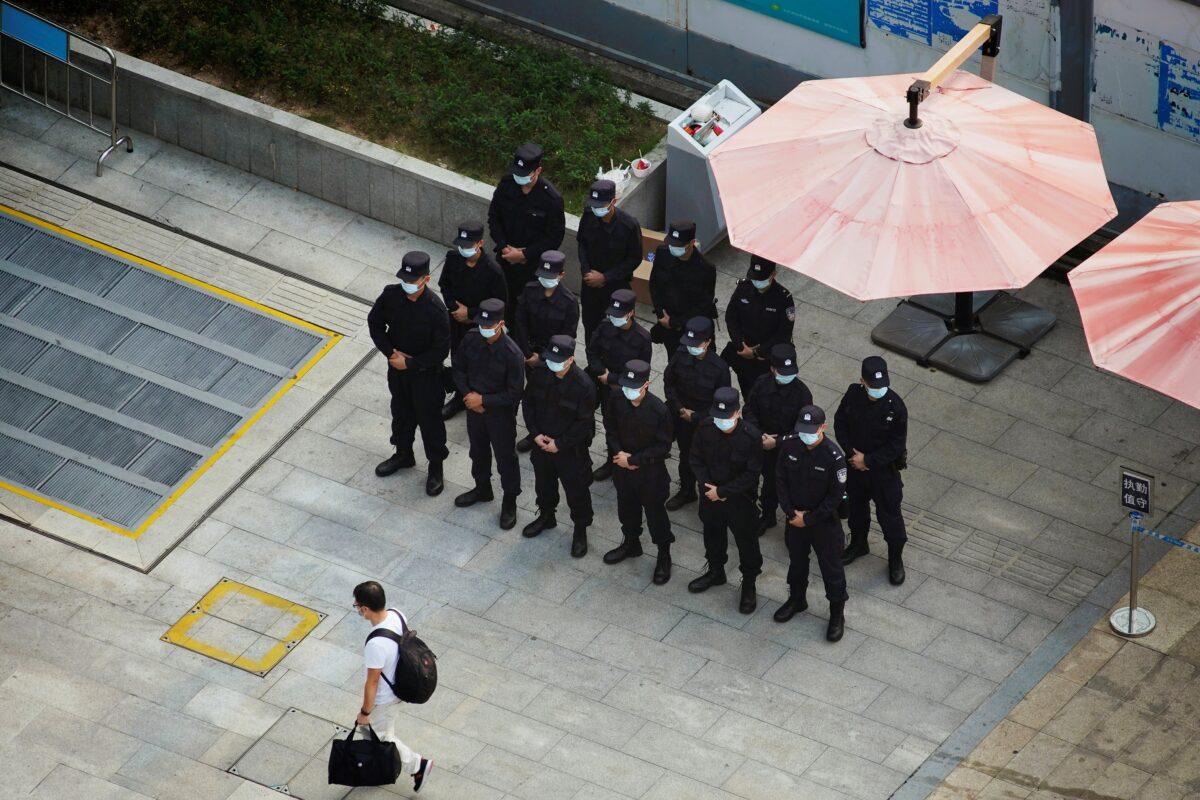A man walks past security personnel standing on duty outside the headquarters of China Evergrande Group in Shenzhen, Guangdong province, China, on Sept. 30, 2021. (Aly Song/Reuters)