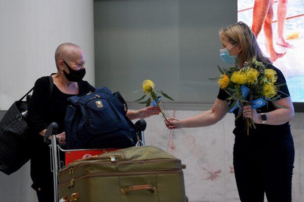 A traveller arriving on the first quarantine free international flight is handed a native Australian flower by an airport worker at Sydney International Airport on Nov. 1, 2021. (AAP Image/Bianca De Marchi)