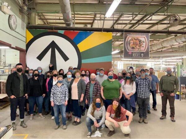 Karen 'Kay Sea' Skau (to the right of the arrow, back row) poses with fellow masked employees in a group photo at JK Adams facility in Dorset, Vt. (Courtesy of JK Adams Facebook Page)