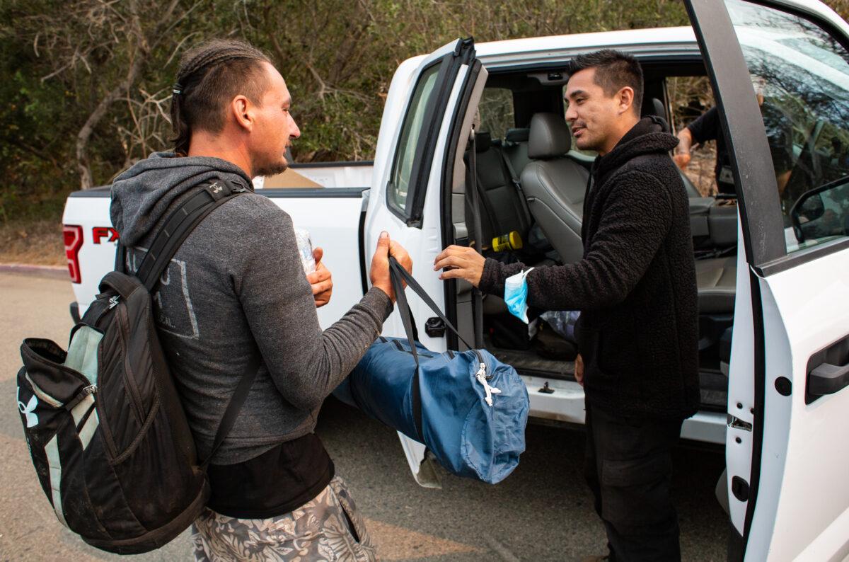 LAHSA team member Shane True gives Jon, a homeless man living within the brush of Zuma Beach, Calif., a tent and a sleeping bag while Los Angeles Sheriff's Department officers offer Jon housing and travel to return to family members in other states, on Sept. 24, 2021. (John Fredricks/The Epoch Times)
