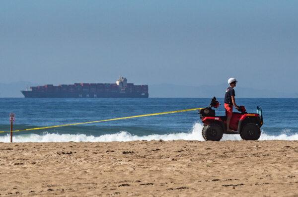 A cargo ship waits to port off the coast of Huntington Beach, Calif., as a Huntington Beach Lifeguard tapes off the beach due to an oil spill, on Oct. 5, 2021. (John Fredricks/The Epoch Times)