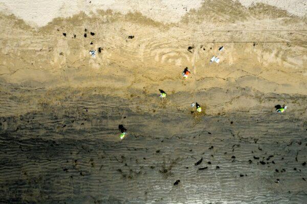In this aerial image taken with a drone, workers in protective suits clean the contaminated beach after an oil spill in Newport Beach, Calif., on Oct. 6, 2021. (Ringo H.W. Chiu/AP Photo)